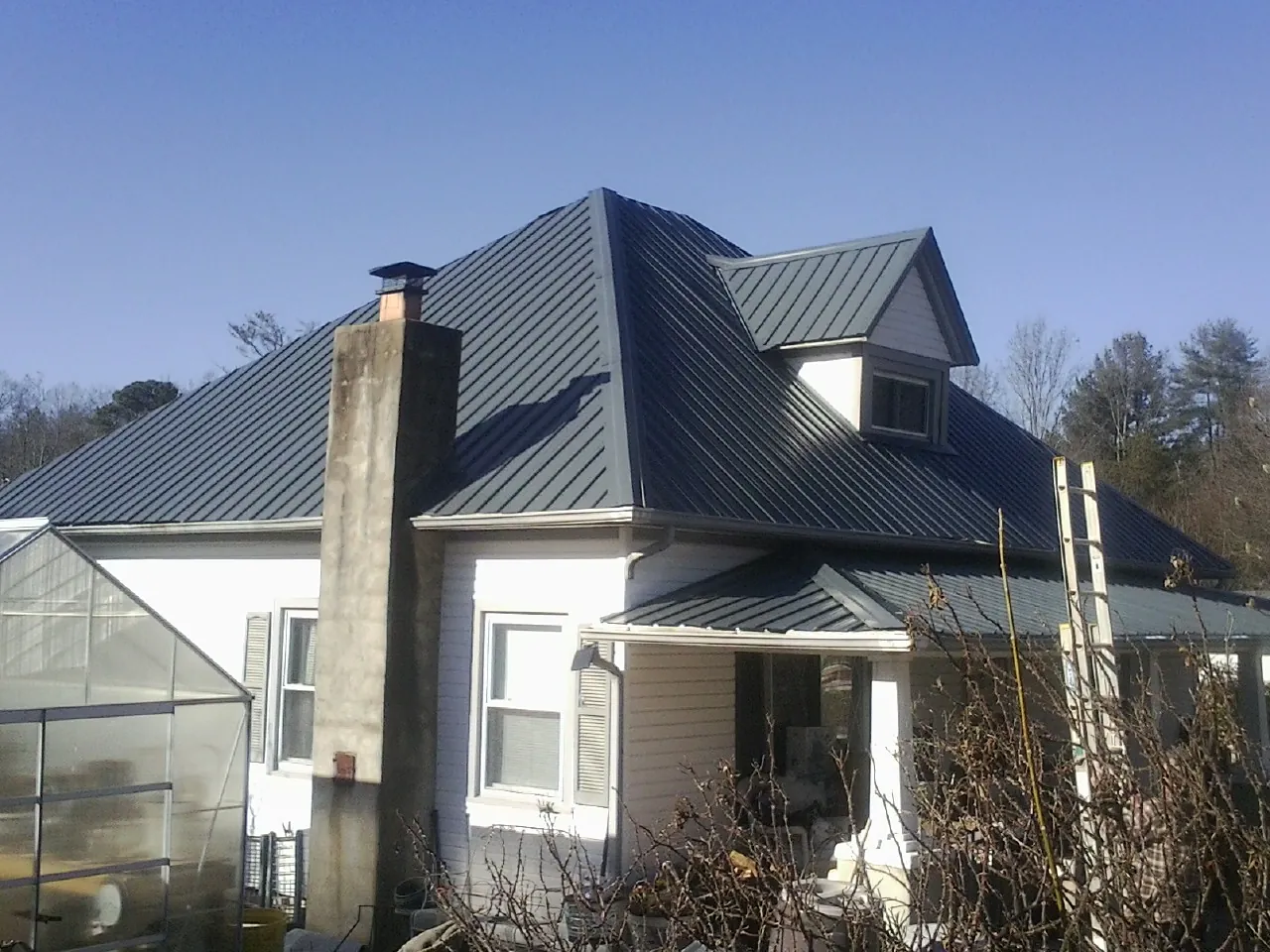 Dark blue standing seam metal roof on a white farmhouse with dormer — Slate & Tile Roof Repair by Roofing Brothers in Sylmar