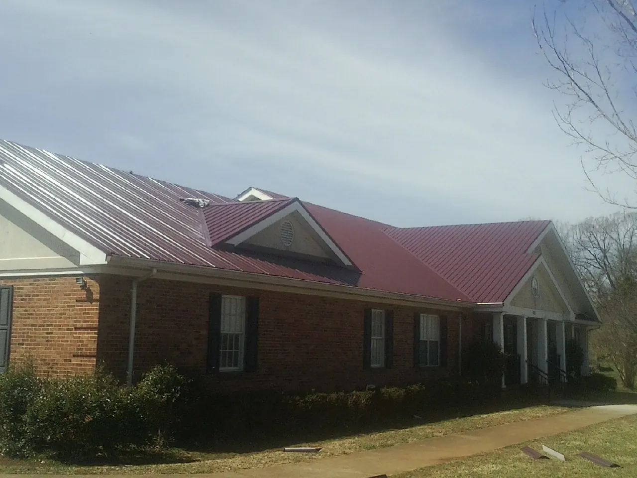 Red metal roof with gabled entries on a long brick building, from a Hail Damage Roof Repair job in Sylmar