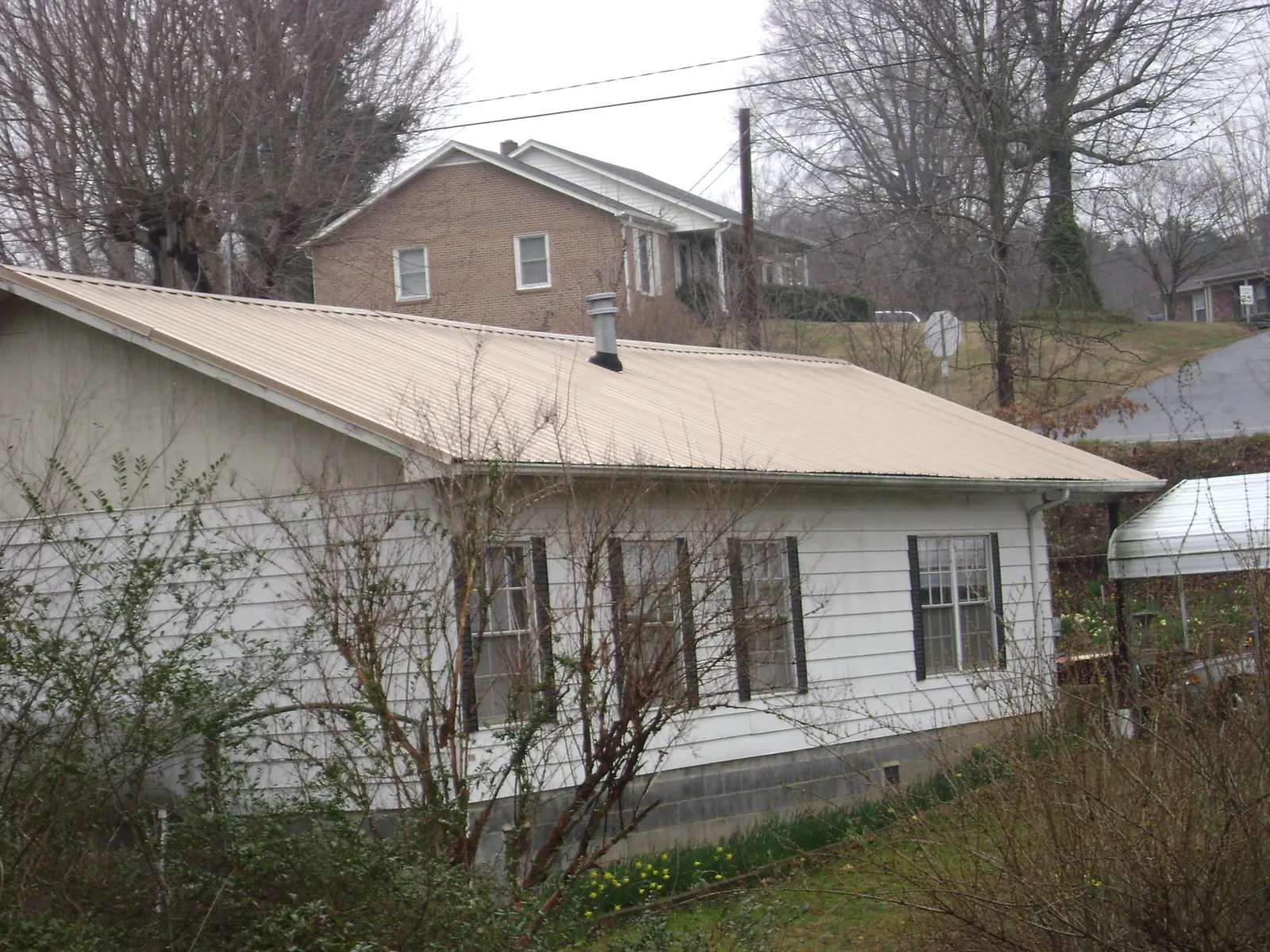 Tan metal roof on a white sided house set into a hillside — Commercial Roofing by Roofing Brothers in Sylmar